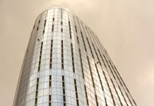 Glass skyscraper with window cleaners scaling the facade against a cloudy sky.