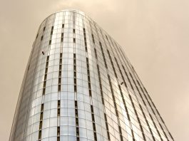 Glass skyscraper with window cleaners scaling the facade against a cloudy sky.