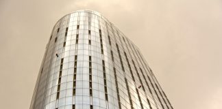 Glass skyscraper with window cleaners scaling the facade against a cloudy sky.