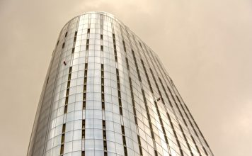 Glass skyscraper with window cleaners scaling the facade against a cloudy sky.