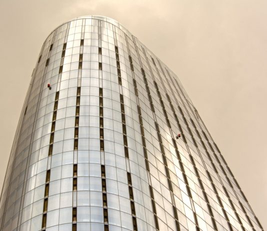 Glass skyscraper with window cleaners scaling the facade against a cloudy sky.
