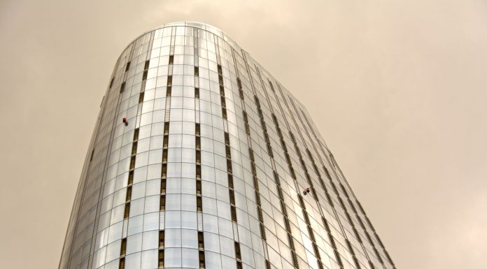Two Climbers Scale Empire State Building With Peace Banner, Proposal and Arrest Follow Glass skyscraper with window cleaners scaling the facade against a cloudy sky.