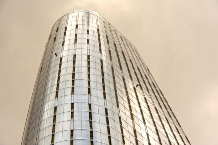 two-climbers-scale-empire-state-building-with-peac Glass skyscraper with window cleaners scaling the facade against a cloudy sky.