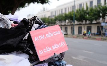 Clothes donation on city street with sign offering free items to those in need.