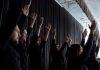 A dynamic group performance with raised arms and synchronized movements indoors.