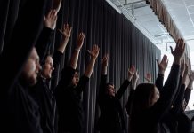 A dynamic group performance with raised arms and synchronized movements indoors.