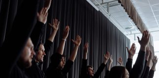 A dynamic group performance with raised arms and synchronized movements indoors.
