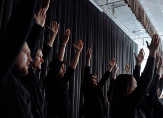A dynamic group performance with raised arms and synchronized movements indoors.