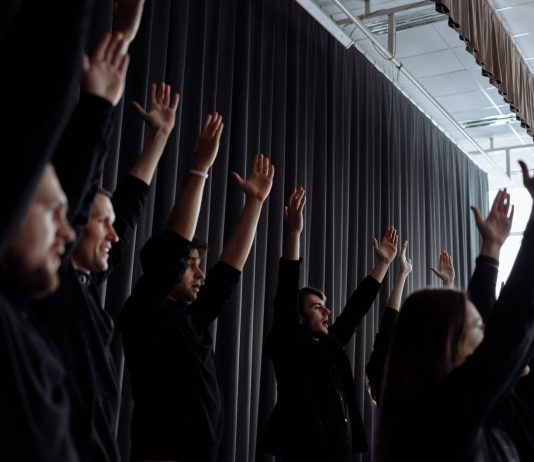 A dynamic group performance with raised arms and synchronized movements indoors.