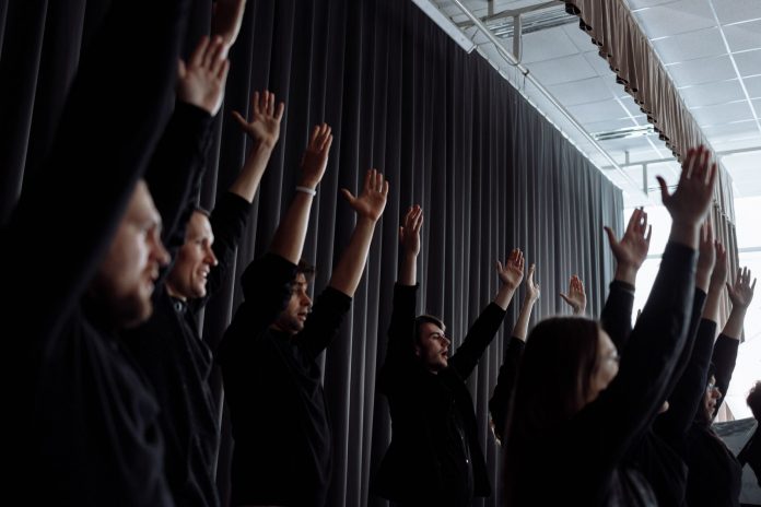 A dynamic group performance with raised arms and synchronized movements indoors.