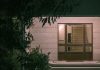 A serene nighttime view of a modern building entrance with surrounding foliage, creating a warm and inviting atmosphere.