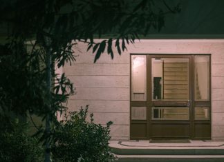 A serene nighttime view of a modern building entrance with surrounding foliage, creating a warm and inviting atmosphere.
