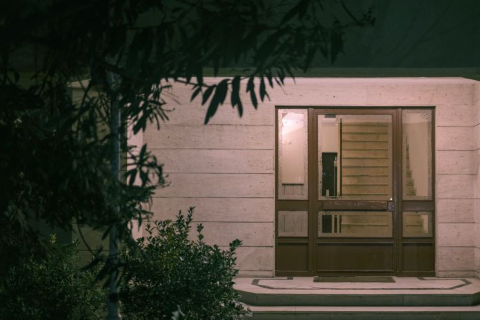 A serene nighttime view of a modern building entrance with surrounding foliage, creating a warm and inviting atmosphere.