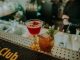 Your guide to the week’s best events in Hudson County Two vibrant cocktails on a bar counter showcasing a sophisticated nightlife atmosphere.