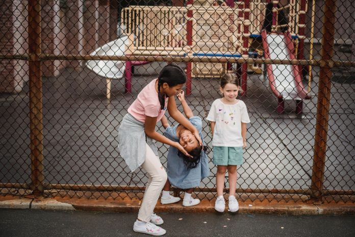 Children having fun at a playground, playing around a fence, enjoying summer day.