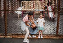 Children having fun at a playground, playing around a fence, enjoying summer day.