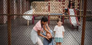Children having fun at a playground, playing around a fence, enjoying summer day.