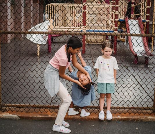 Children having fun at a playground, playing around a fence, enjoying summer day.
