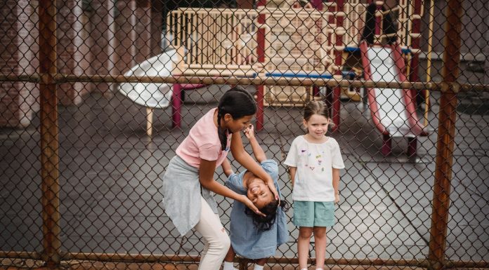 Children having fun at a playground, playing around a fence, enjoying summer day.