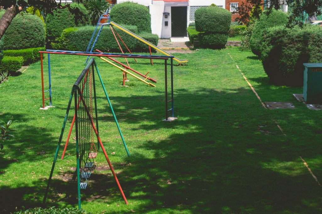 Vibrant outdoor playground with swings and slides in a lush green park setting under a bright sky.