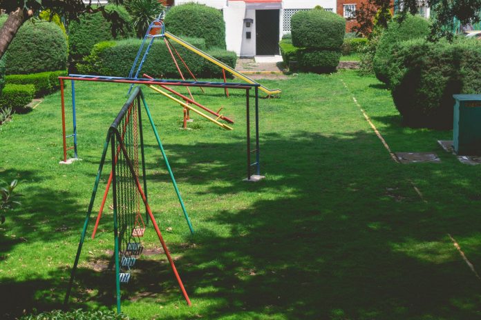 Vibrant outdoor playground with swings and slides in a lush green park setting under a bright sky.