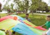 Kids enjoying a fun outdoor game with a colorful parachute and ball in a park setting.