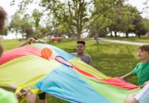Kids enjoying a fun outdoor game with a colorful parachute and ball in a park setting.