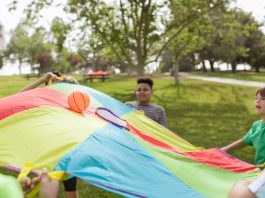 Kids enjoying a fun outdoor game with a colorful parachute and ball in a park setting.