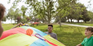 Kids enjoying a fun outdoor game with a colorful parachute and ball in a park setting.