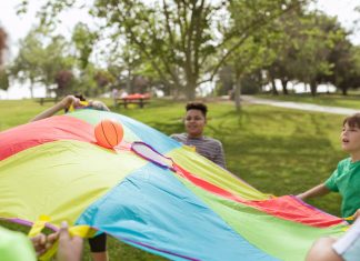 Autism Summer Camp Gives Hudson Families a Respite Kids enjoying a fun outdoor game with a colorful parachute and ball in a park setting.