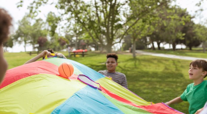 Autism Summer Camp Gives Hudson Families a Respite Kids enjoying a fun outdoor game with a colorful parachute and ball in a park setting.