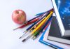 Colorful school supplies arranged with an apple on a white surface, ideal for education themes.