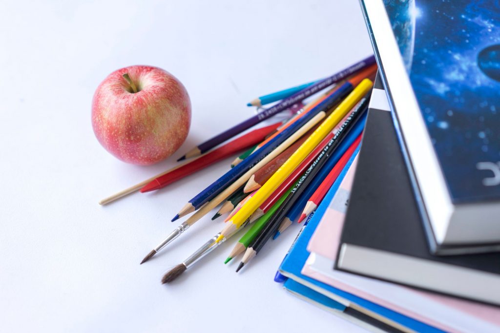 Colorful school supplies arranged with an apple on a white surface, ideal for education themes.