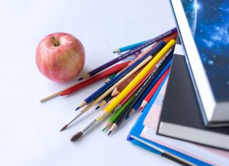Colorful school supplies arranged with an apple on a white surface, ideal for education themes.