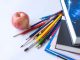 Colorful school supplies arranged with an apple on a white surface, ideal for education themes.