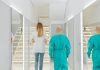 Two medical practitioners walking down a bright clinic hallway with reflections in mirrors.