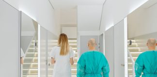 Two medical practitioners walking down a bright clinic hallway with reflections in mirrors.
