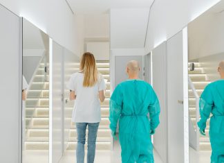 Two medical practitioners walking down a bright clinic hallway with reflections in mirrors.