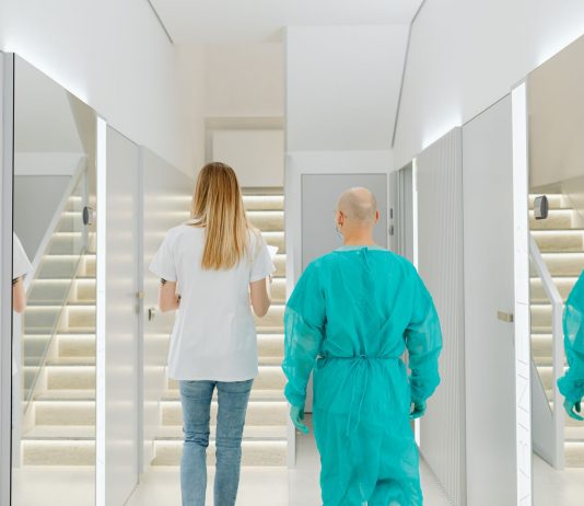 Two medical practitioners walking down a bright clinic hallway with reflections in mirrors.