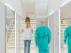 Baker Health Wellness Practice Opening in Hoboken Two medical practitioners walking down a bright clinic hallway with reflections in mirrors.