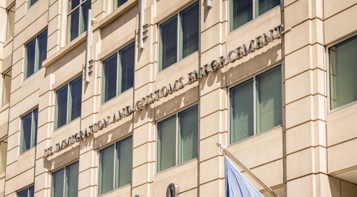 Exterior view of the US Immigration and Customs Enforcement building with a visible flag and signage.