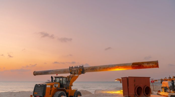 Dramatic view of beach construction site with heavy machinery at sunset.