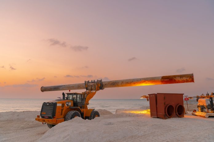 Dramatic view of beach construction site with heavy machinery at sunset.