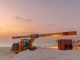 Dramatic view of beach construction site with heavy machinery at sunset.