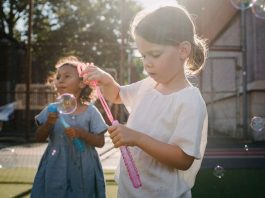 Two children joyfully creating bubbles, enjoying outdoor play under the sun.
