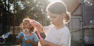 Two children joyfully creating bubbles, enjoying outdoor play under the sun.