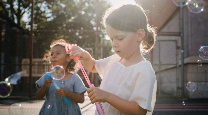 Two children joyfully creating bubbles, enjoying outdoor play under the sun.