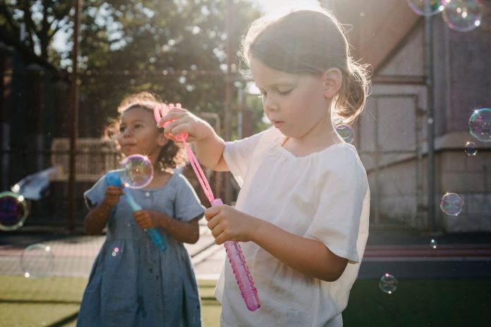 Two children joyfully creating bubbles, enjoying outdoor play under the sun.