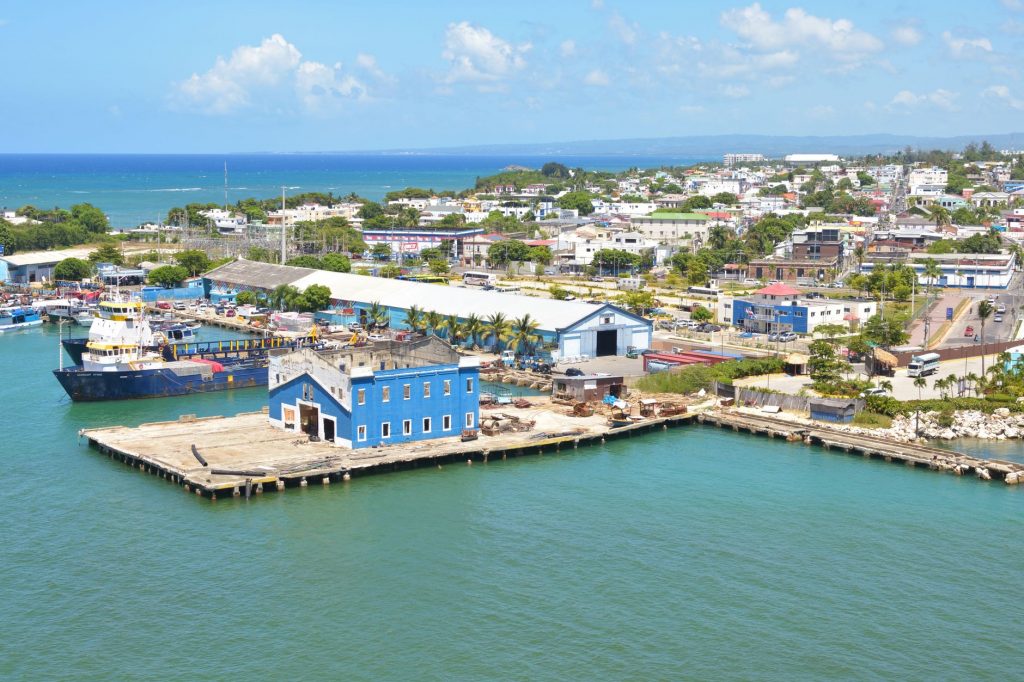 Aerial view of Puerto Plata harbor with blue buildings, ships, and a coastal town in the Dominican Republic.