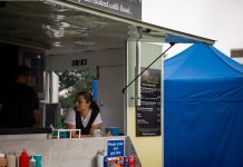 A food truck with staff serving at an outdoor festival with colorful tents.